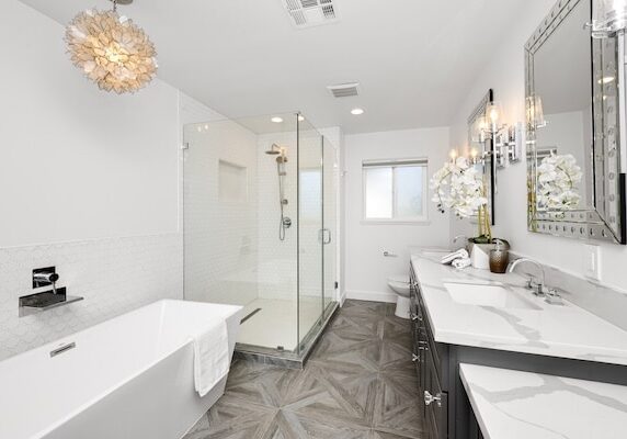 Elegant modern bathroom with wooden floors, marble counters, white tub, and two sinks